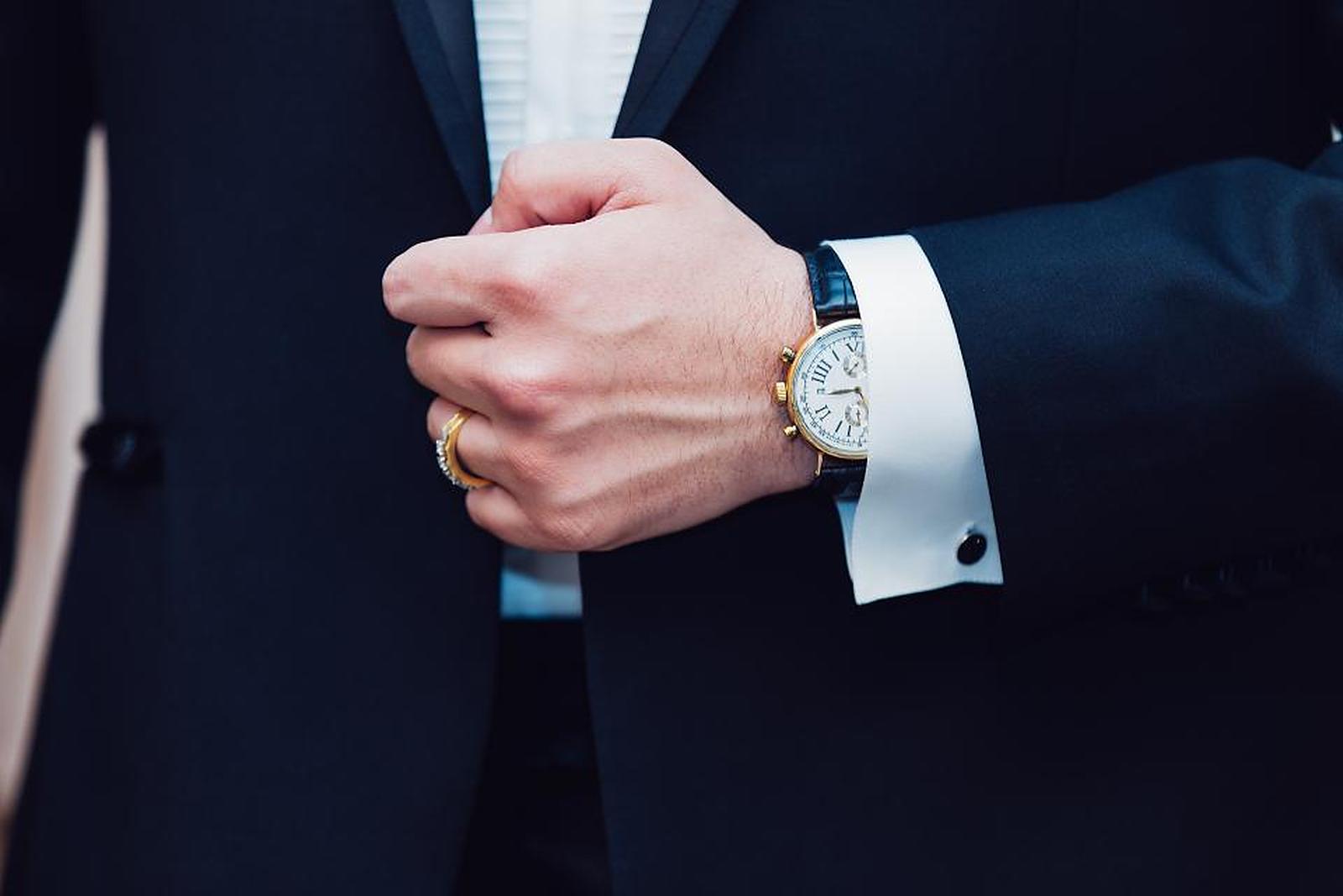 A man in a dark suit fastening his cufflinks
